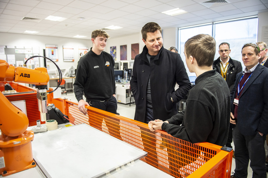 AMRC Training Centre apprentices give a robotics demonstration to George Clarke, programming the robot to write out 'Welcome George'.