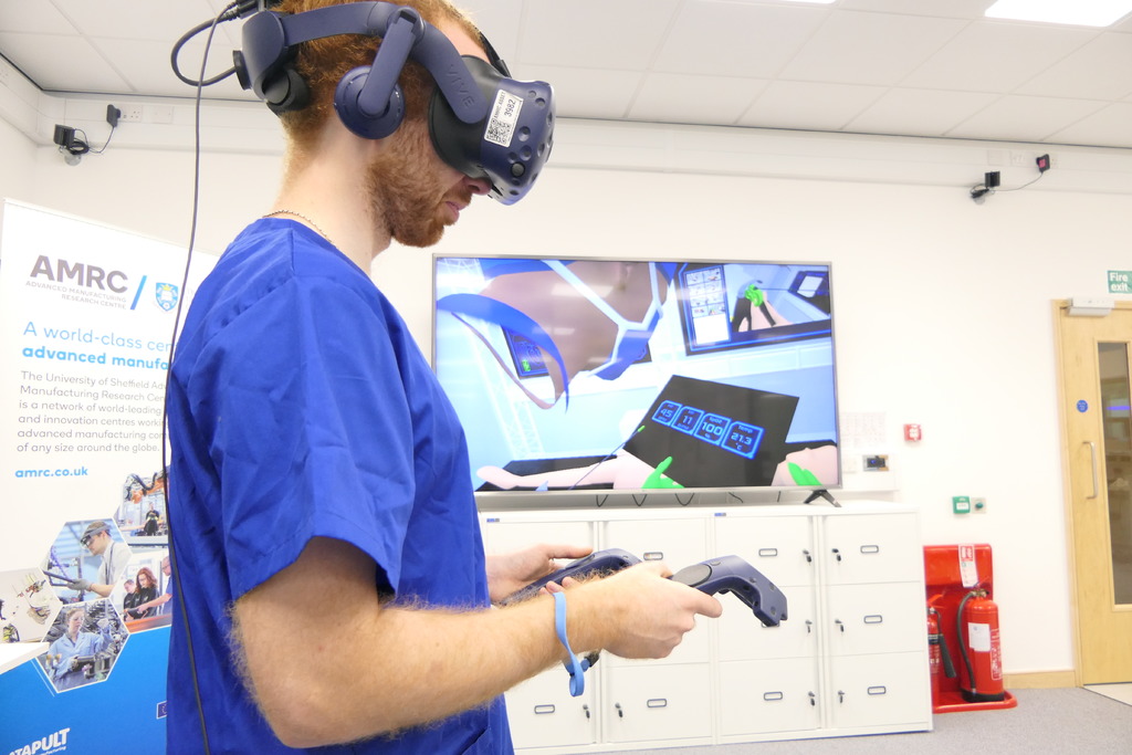 Project engineer Rob Stacey wears a virtual reality headset with his avatar in the Digital Operating Theatre shown on the screen behind him.